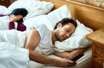 Flaute im Bett? So bringen Sie neuen Schwung ins Schlafzimmer Paar im Bett. Mann mit Handy