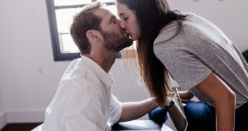 Work-Love-Balance – So bringt ihr euer Liebes- und Arbeitsleben in Einklang Paar küsst sich liebevoll, während er am Laptop arbeitet