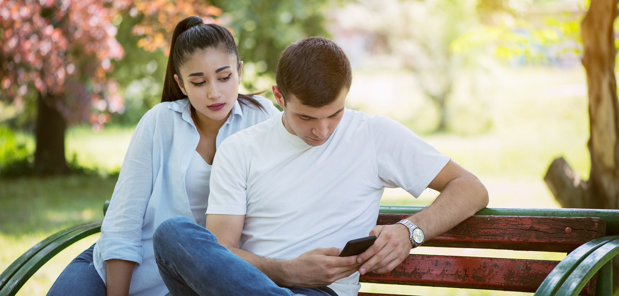 Frau schaut heimlich auf das Handy von ihrem Partner, während er es bedient