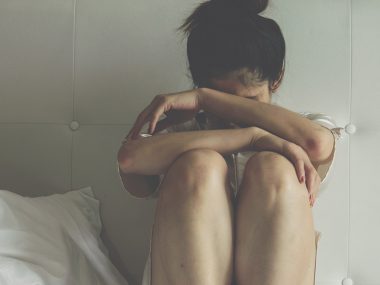 Frau sitzt bedrückt auf dem Bett